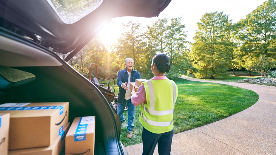 Woman in a yellow vest handing an Amazon package to a customer in a rural driveway