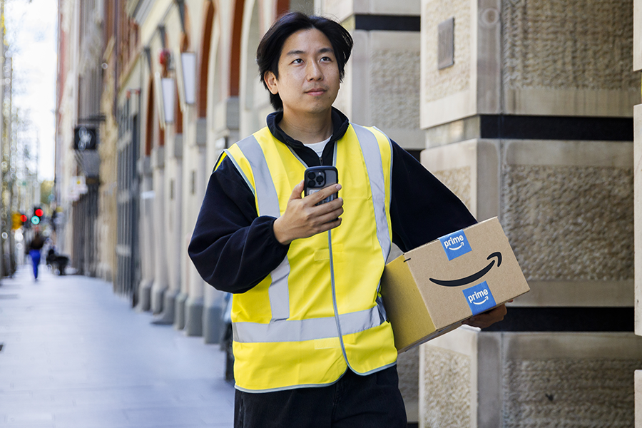  Man in a yellow vest holding an Amazon package and smartphone walking on an urban street