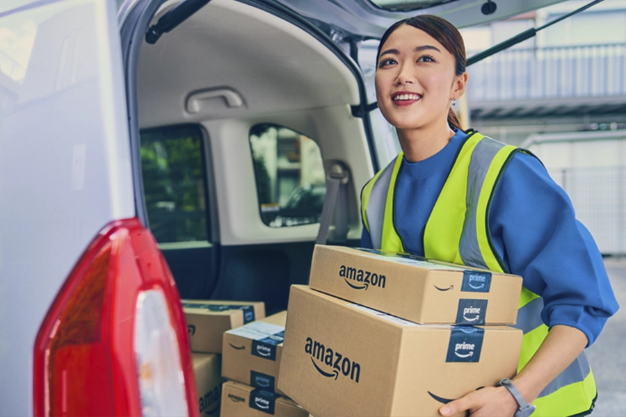 Woman in yellow vest unloading two Amazon packages from her vehicle in an urban setting